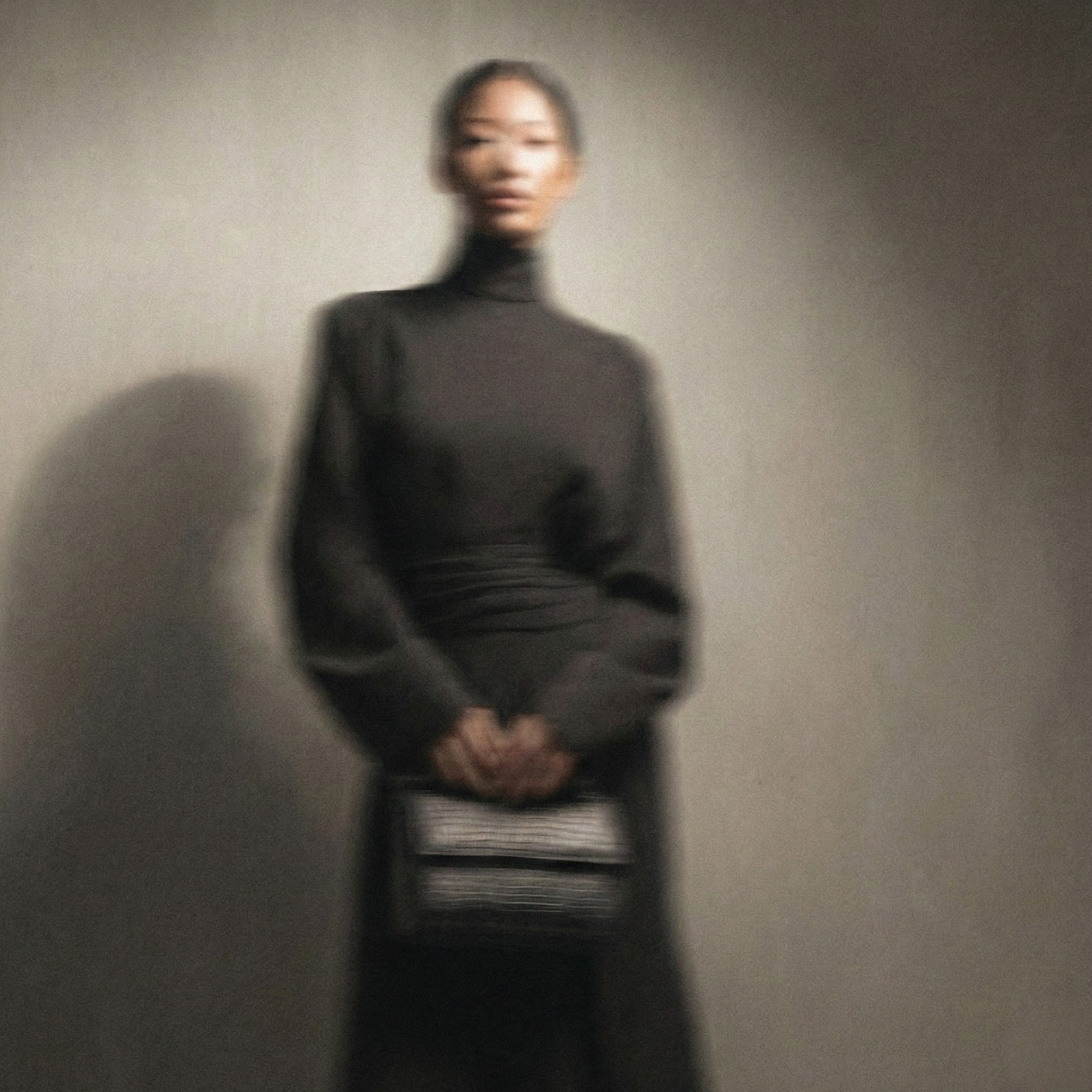 Person wearing a dark turtleneck and holding a book against a plain background