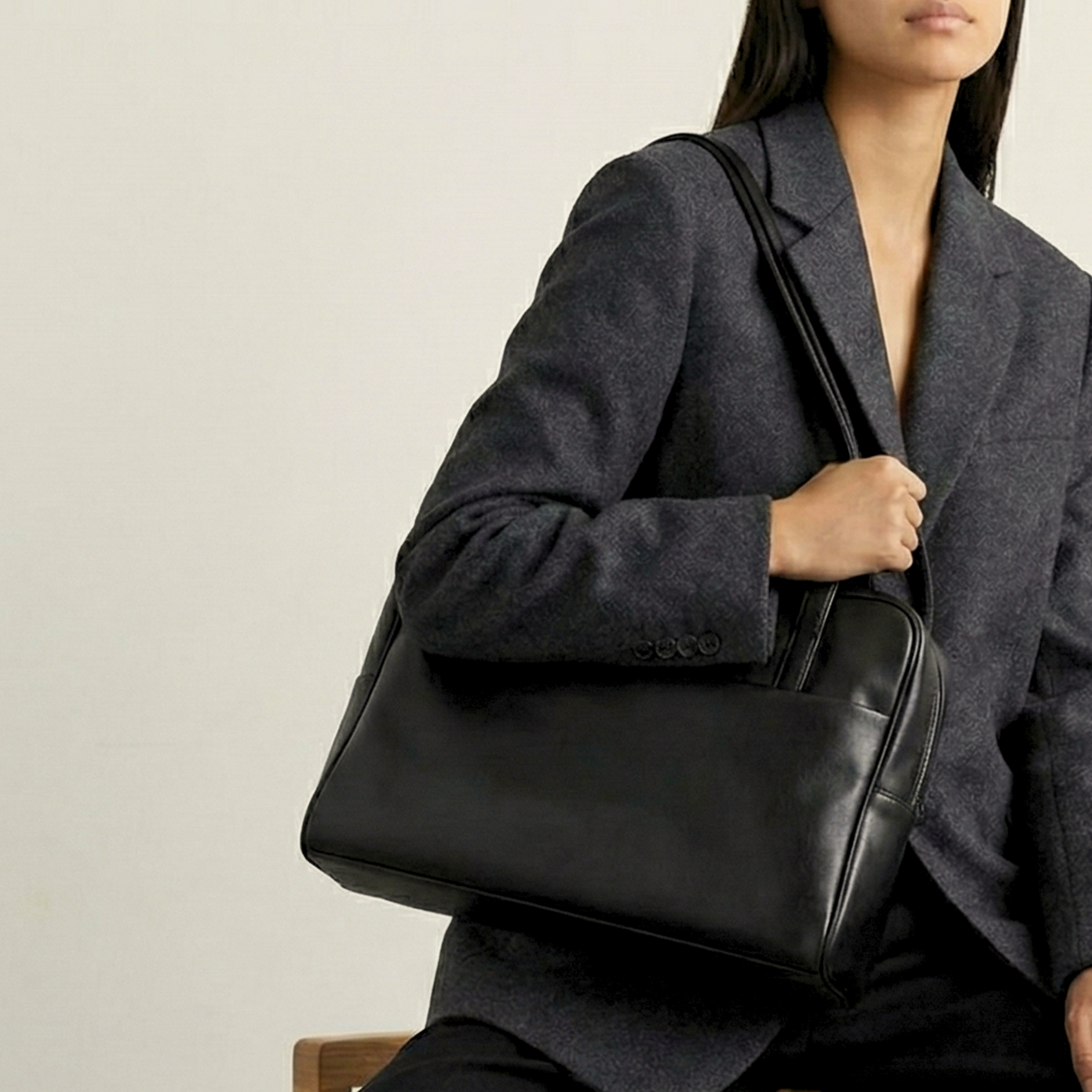 Person holding a black leather bag against a neutral background