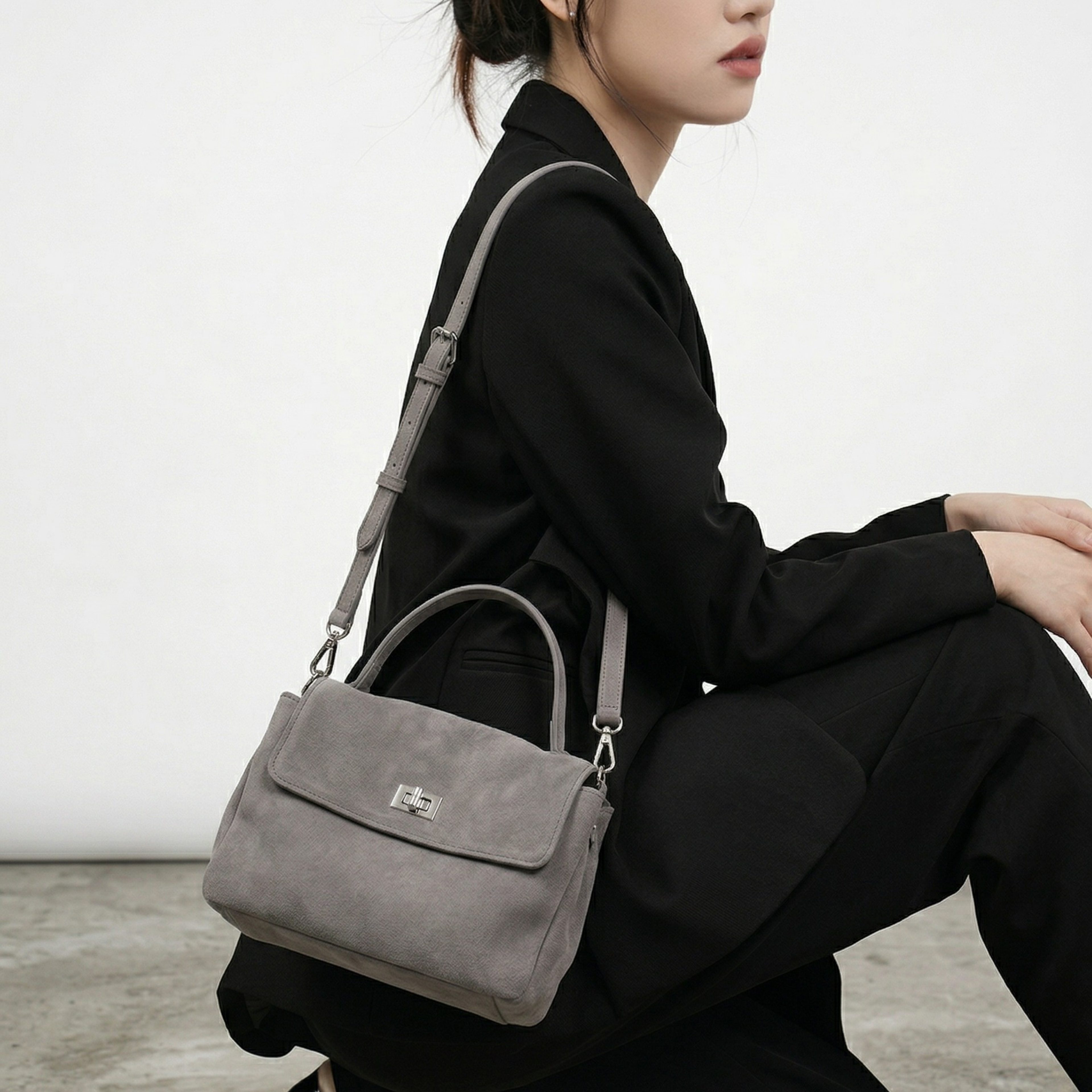 Person wearing a gray handbag with a visible brand logo on a neutral background