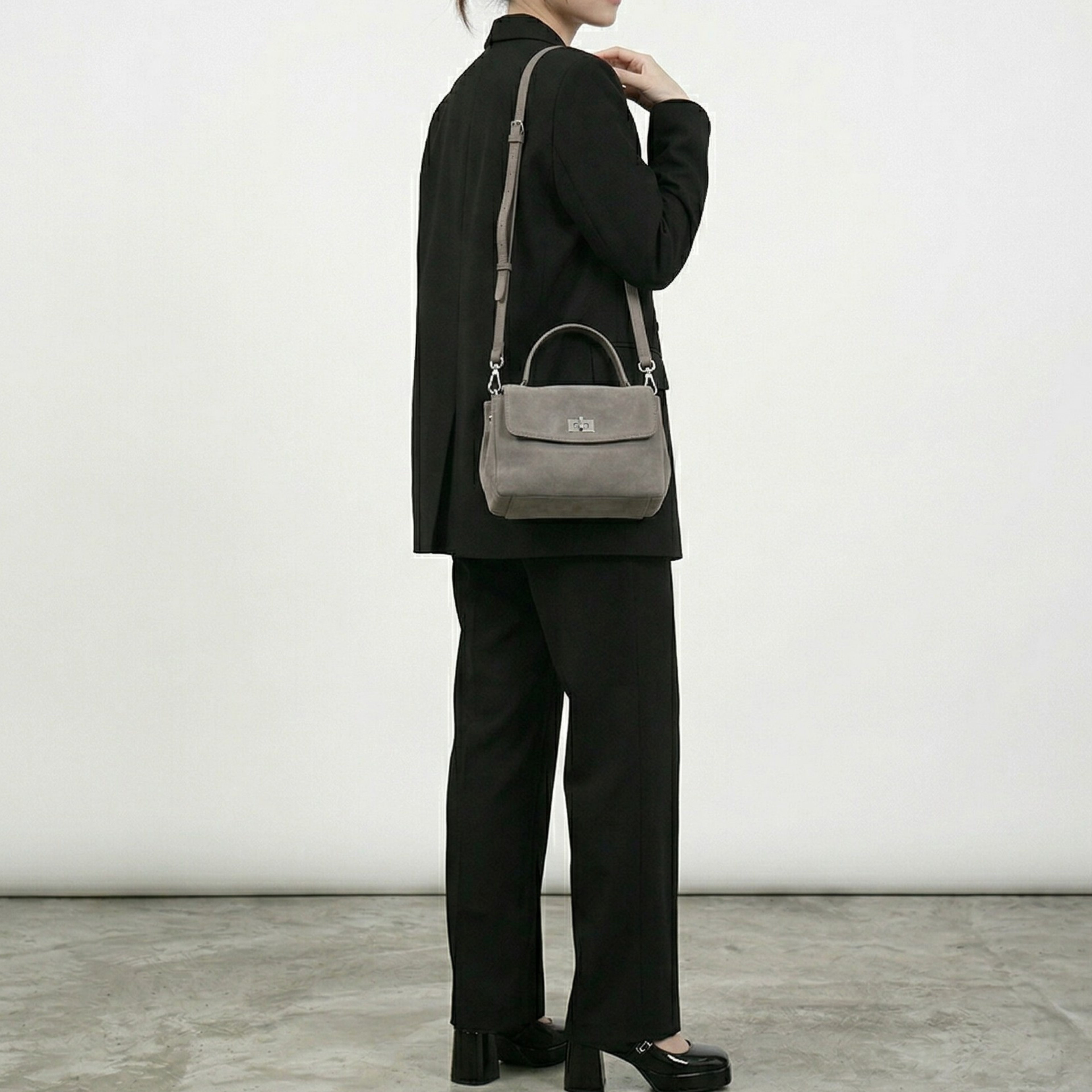 Person wearing a black outfit with a gray handbag against a white background