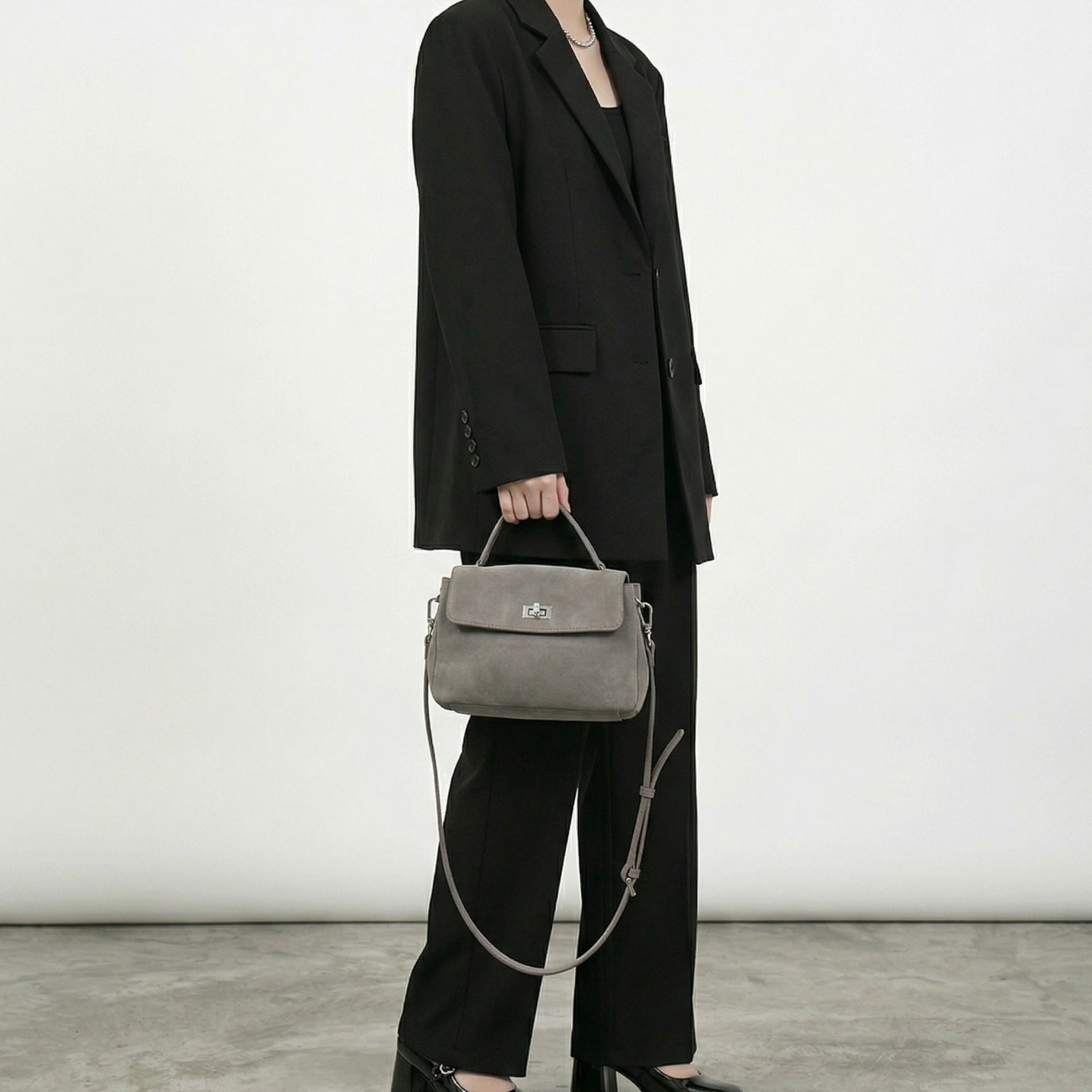 Person wearing a black suit holding a gray handbag against a white background