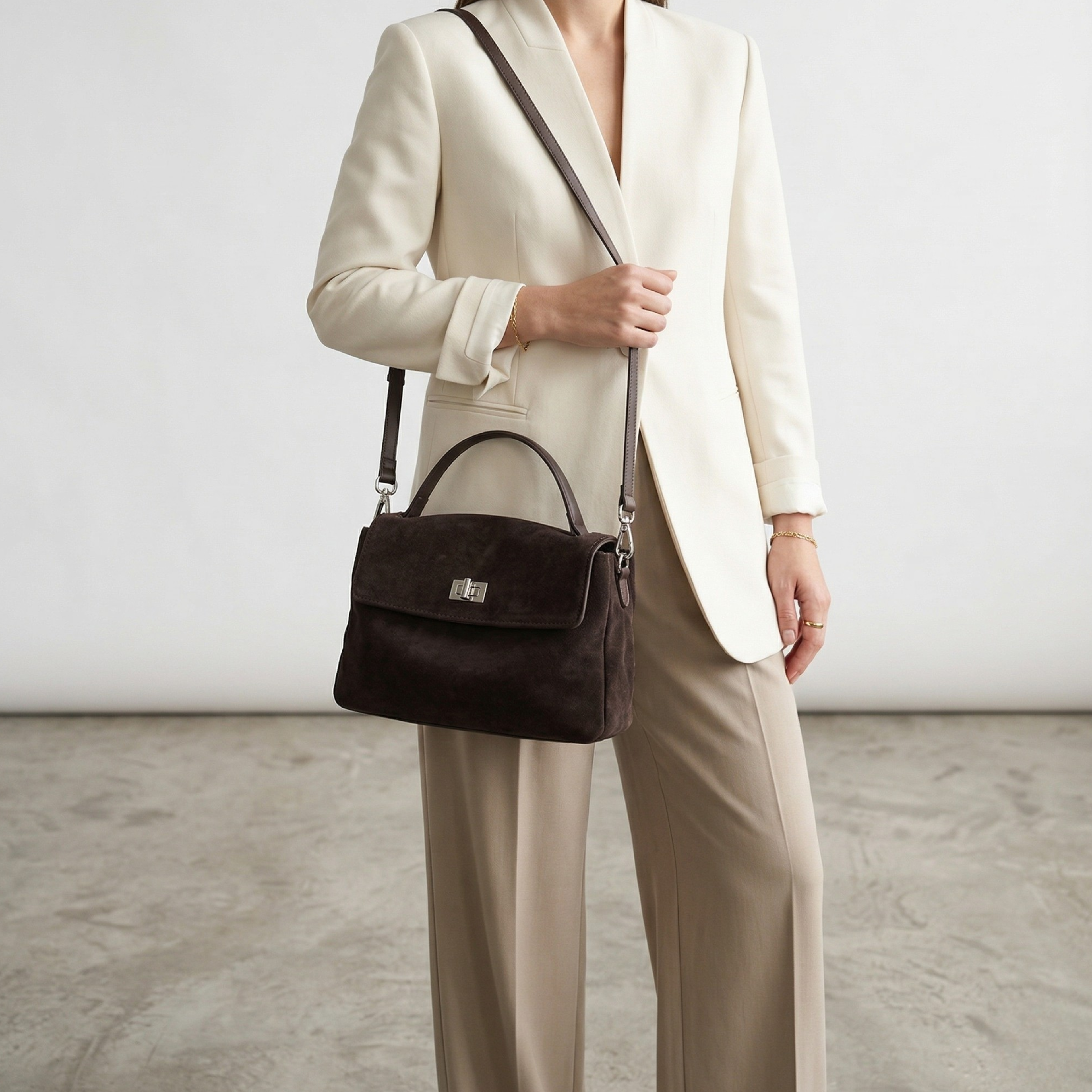 Person wearing a beige suit with a brown handbag on a neutral background