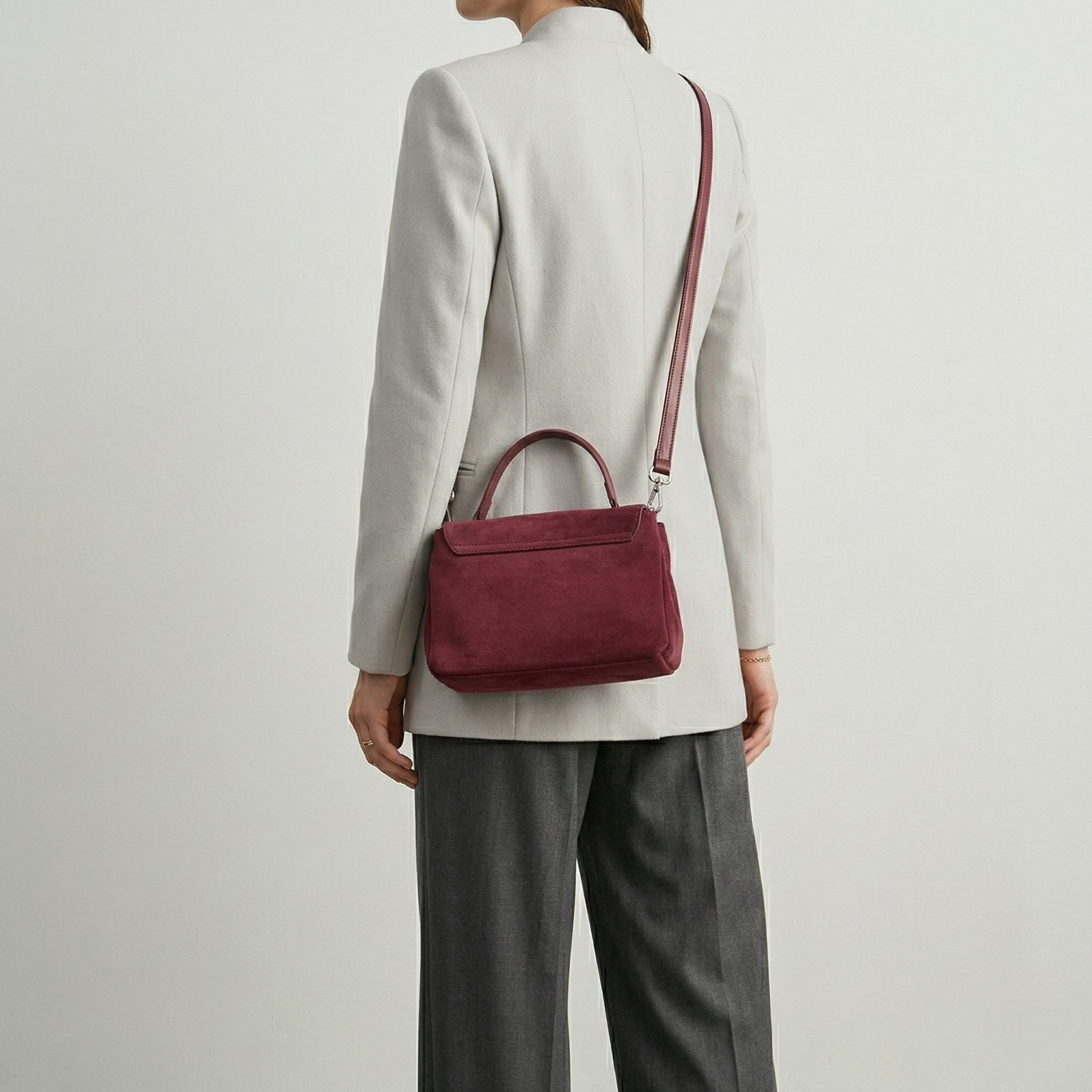 Person wearing a burgundy handbag over one shoulder on a plain background
